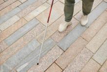 Image of a brick floor and a student's lower legs and feet and who is holding a cane due to a visual impairment.